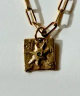 Collar de plata con cadena de eslabones alargados y dije de medalla rectangular con textura rústica, grabado en relieve con forma de estrella y una piedra brillante incrustada en el centro.