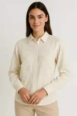 Camisa de manga larga color crema, con cuello camisero y botones frontales. Presenta bordados florales en relieve en el frente y puños abotonados.