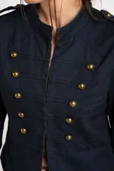 Chaqueta corta color beige de algodón, de inspiración militar con cuello mao y doble botonadura frontal con botones metálicos dorados.