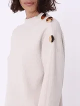 Sweater color beige de tejido de punto, con cuello redondo y mangas largas. Detalle de botones dorados en el hombro.