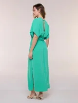 Vestido largo amarillo de corte fluido con escote en V, mangas cortas amplias y apliques de tachas en el escote y puños. Posee cintura elastizada fruncida y falda larga con tajos laterales en el ruedo.