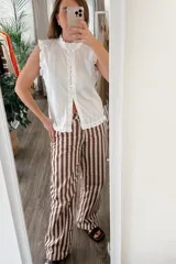 Blusa blanca sin mangas con cuello mao y volados en hombros y ruedo. Cierre frontal con botones.