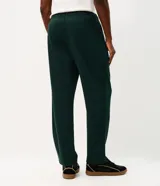 Pantalón deportivo de corte recto color verde oscuro, confeccionado en tejido de algodón y poliéster. Cuenta con cintura elástica con cordón ajustable, bolsillos laterales funcionales y una cinta decorativa lateral.