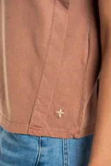 Remera de algodón color mostaza/naranja quemado, con cuello redondo y mangas cortas. Presenta un diseño con costuras externas visibles en los hombros y laterales, dándole un aspecto desestructurado.