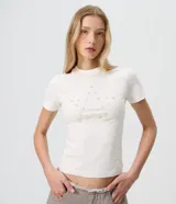 Remera de algodón con elastano color blanco, de corte ajustado, manga corta y cuello redondo. Presenta un detalle frontal de botones dispuestos en forma de estrella.