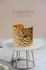 Brazalete ancho de diseño abierto con textura martillada y acabado brillante en tono dorado.