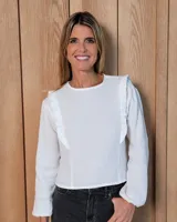 Blusa de manga larga color blanco, con cuello redondo y detalle de volados verticales en los hombros. Confeccionada en tejido de textura ligera.