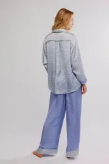 Conjunto de pijama de dos piezas, compuesto por una camisa de manga larga con estampado geométrico, cuello y botonadura frontal, y un pantalón largo fluido de color celeste con cintura elastizada, cordón de ajuste y detalles estampados en los dobladillos.