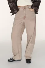 Jeans de tiro medio, color beige rosado con efecto lavado, corte amplio (baggy balloon) y detalle de costuras torcidas en el frente de las piernas.