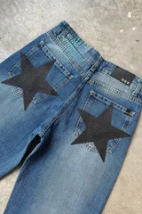 Jean de mezclilla azul de corte recto y tiro medio, con un gran parche negro en forma de estrella en el bolsillo trasero.
