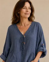 Blusa color azul jean con escote en V, cierre frontal con botones de madera y cordones ajustables, mangas largas con presilla y bolsillos delanteros con detalles desflecar.