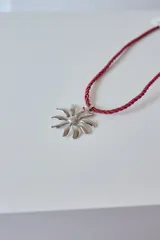 Collar con tiento trenzado color crema y dije de acero quirúrgico hipoalergénico con forma de sol o flor estilizada.