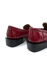 Mocasín de cuero color cereza con apliques metálicos plateados en la parte delantera, suela plana y taco cuadrado bajo color negro.