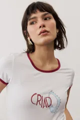 Remera blanca de manga corta ajustada al cuerpo, con ribetes en color bordo en el cuello y las mangas. Cuenta con un estampado frontal con texto y un diseño abstracto.