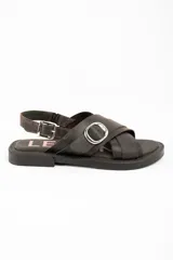 Sandalias de cuero marrón oscuro, con tiras cruzadas en el empeine, hebilla metálica grande decorativa y tira ajustable en el talón con hebilla plateada.