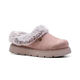 Zueco tipo pantufla de diseño casual, confeccionado con parte superior textil de aspecto gamuzado en color rosado. Presenta un interior y ribete de piel sintética, suela de plataforma plana con absorción de impactos y un pequeño aplique metálico en forma de corazón en el lateral.
