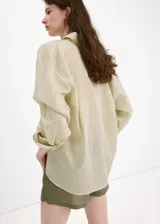 Camisa oversize color beige con sutiles rayas verticales, cuello camisero y cierre frontal con botones.