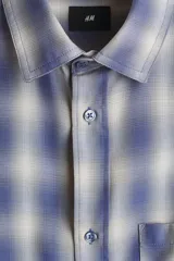 Camisa de manga larga con ajuste relajado, cuello inglés y un bolsillo aplicado en el pecho. Presenta cierre frontal de botones y bajo redondeado.