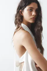 Top blanco de tejido satinado con cuello halter drapeado ajustable con lazada en el cuello y espalda descubierta con lazada.