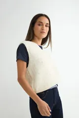 Chaleco de punto color crema con escote en V, sin mangas y diseño decorado con pequeñas perlas aplicadas en toda la superficie.