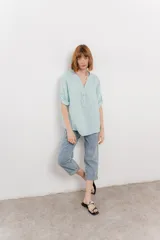 Camisa color topo confeccionada en lino, de corte holgado, con escote en V abotonado, bolsillo frontal y mangas 3/4 arremangables.