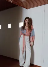 Blusa de manga larga con estampado de rayas en tonos rosados y celestes, cuello camisero, cierre frontal con botones y detalle de lazada lateral en la cintura.