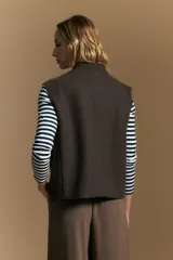 Chaleco de paño color marrón oscuro, de silueta recta y diseño minimalista. Presenta cuello a la base, cierre frontal con botones claros y bolsillos aplicados.