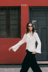 Blusa de lino color crudo, con cuello alto y lazo decorativo frontal. Presenta mangas largas con corte acampanado y diseño entallado con pinzas delanteras.