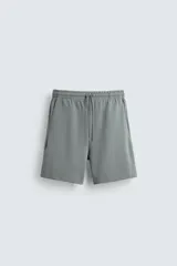 Bermuda de algodón color beige claro, corte relajado (relaxed fit), con cintura elástica ajustable mediante cordón y bolsillos laterales y trasero de plastrón.