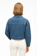 Chaqueta corta color beige con doble botonadura, cuello solapa, cinturón con hebilla rectangular y mangas largas con puños elásticos.