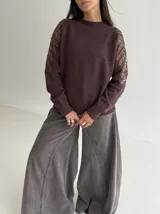 Sweater de punto color marrón chocolate, con cuello redondo y mangas largas que presentan detalles de transparencias y apliques bordados con pedrería.