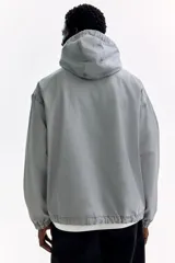 Campera popover de algodón color gris con efecto lavado, cuello elevado, capucha con cordón ajustable, medio cierre y bolsillo frontal con solapa.