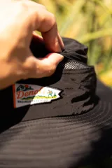 Sombrero negro tipo pescador con ala ancha, cordón ajustable naranja y parche frontal con logo de la marca Denali.