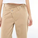 Pantalón de twill color beige con diseño de cintura asimétrica cruzada y corte recto de pierna ancha.