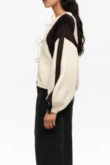 Cardigan de punto con diseño de bloques de color en blanco, negro y marrón, escote redondo y cierre frontal con múltiples lazos de tela.