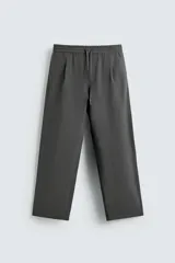 Pantalón de corte relajado, color gris oscuro, con cintura elástica ajustable mediante cordón y pliegues frontales. Presenta bolsillos laterales y bolsillos traseros de parche con pespuntes contrastantes.