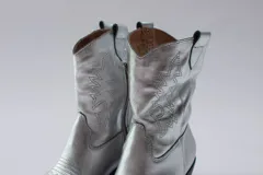 Botas de estilo western (texanas) de caña media, color blanco, confeccionadas en cuero. Presentan bordados decorativos en la caña y puntera cuadrada. Cuentan con cierre lateral y taco de altura media.
