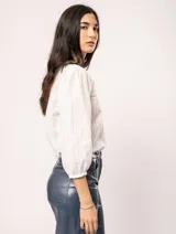 Blusa blanca de algodón con escote redondo, manga tres cuartos y silueta oversized. Presenta bordados y texturas combinadas.