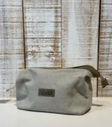 Neceser de tela color gris con cierre superior y aplique de cuero con logo de la marca en el frente.