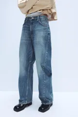 Jeans de tiro medio con diseño baggy barrel, confeccionados en denim color beige con efecto lavado. Presentan cinco bolsillos, costuras laterales torcidas y cierre frontal con cremallera y botón metálico.