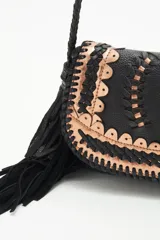 Cartera bandolera negra de cuero con diseño trenzado y apliques dorados en el frente, flecos de cuero en la parte inferior y correa trenzada.
