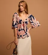 Blusa azul marino con estampado floral en tonos rojo y blanco, escote en pico con nudo y mangas cortas fruncidas.