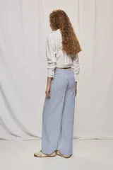 Pantalón de pierna ancha y tiro medio con diseño de rayas verticales blancas y azules. Cuenta con bolsillos delanteros amplios y cierre frontal con botón y cremallera.