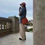 Bandolera negra de cuero sintético con detalles en marrón, cierre superior con cremallera y correa ajustable.