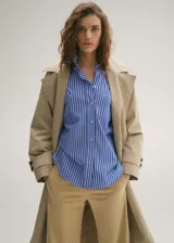 Camisa celeste a rayas verticales blancas, de corte oversize y largo crop. Tiene cuello camisero, cierre frontal con botones, manga larga con puños abotonados y un bolsillo de parche en el pecho.