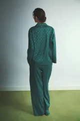 Pijama de dos piezas compuesto por camisa de manga larga con cuello camisero y botones frontales, y pantalón de corte recto y holgado con cintura elástica y cordón de ajuste. Presenta un diseño estampado con pequeños corazones en tono sobre tono.