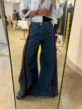 Jean de corte wide leg en denim azul oscuro, con detalle de franja lateral decorativa en color rojo y ruedo deshilachado.