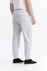 Pantalón de jogging color gris melange, confeccionado en tejido de algodón y poliéster. Presenta cintura elástica con cordón de ajuste, bolsillos laterales con cierre y puños elásticos en los tobillos.