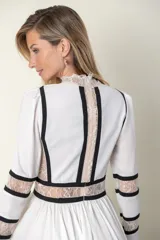 Vestido midi blanco con detalles de encaje y vivos negros. Tiene cuello mao, mangas largas con puños de encaje y falda amplia con tul de armar.