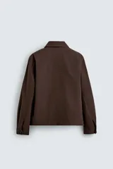 Sobrecamisa de corte regular confeccionada en tejido con estructura canvas color marrón. Presenta un ligero acolchado interior, cuello de solapa y cierre frontal con cremallera metálica. Incluye dos bolsillos de plastrón en el pecho y bolsillos laterales de vivo, con mangas largas terminadas en puños con botón.